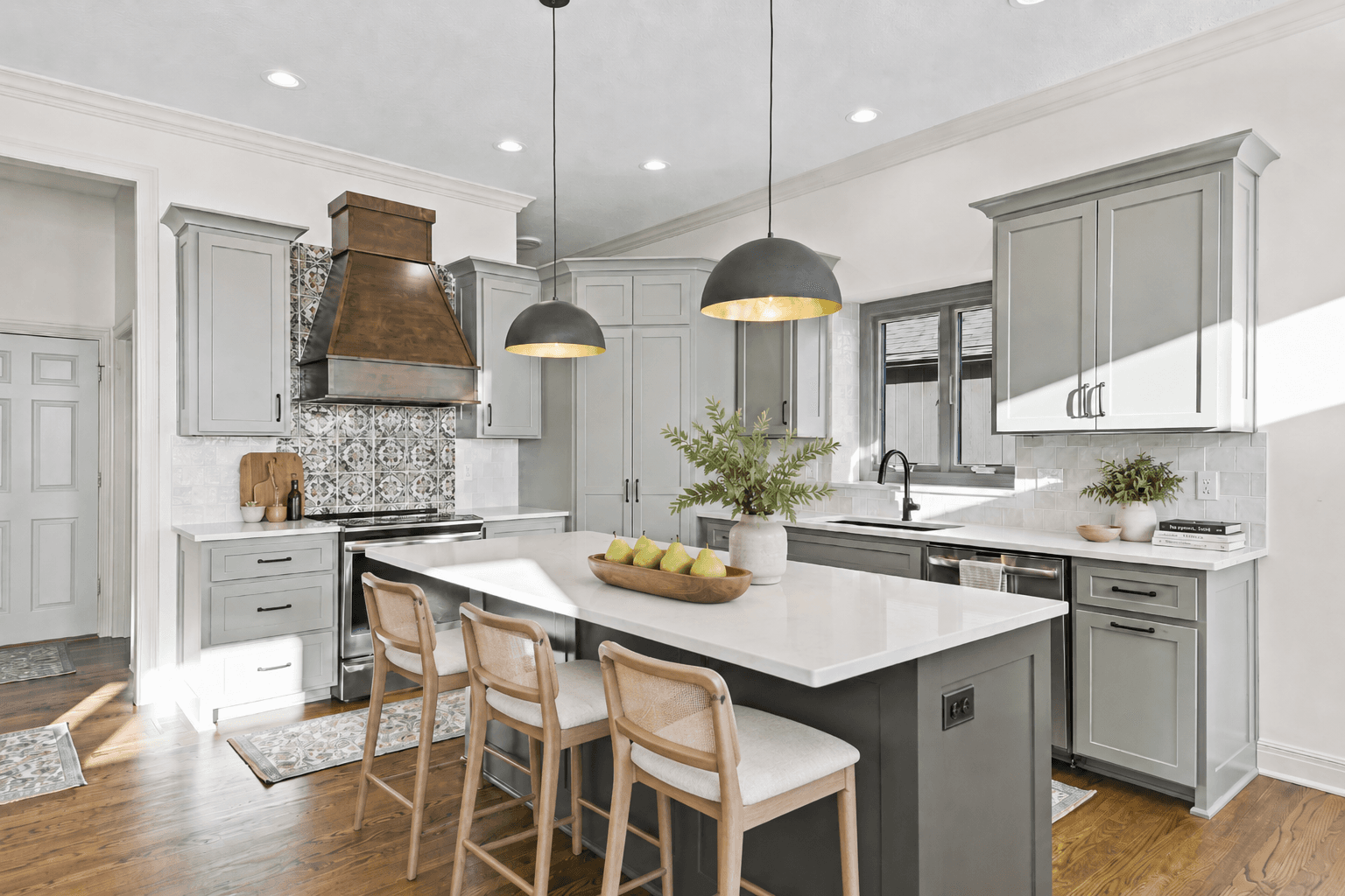 Sage green kitchen with patterned tile, a wood range hood, black pendant lighting, a white island, and light wood stools